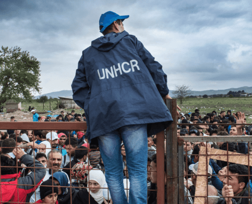 A UNHCR employee talks to refugees as they wait during a rainstorm to enter inside a refugee camp near the town of Gevgelija at the Macedonian